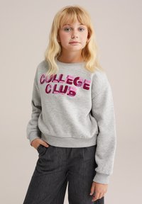 Sivý fleecový sveter s nápisom "COLLEGE CLUB" v ružovom trblietavom písmene, s rebrovanými manžetami a pásom; model nosí tmavé nohavice.