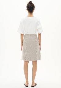 T-shirt blanc surdimensionné à manches courtes, associé à une jupe beige rayée arrive au genou avec une taille bien définie. Sandales noires visibles.
