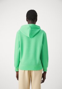 Felpa verde con cappuccio regolabile, tessuto morbido, polsini e orlo a coste. La parte posteriore presenta un design pulito senza loghi o motivi visibili.
