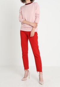 Jasnoróżowy prążkowany sweter w zestawieniu z jasnoczerwonymi spodniami o dopasowanym kroju, z postrzępionymi brzegami, oraz beżowymi butami na obcasie. Prosty fason.