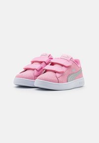 Un paio di sneakers per bambini Puma rosa con doppie fascette in velcro e suole bianche su uno sfondo bianco.