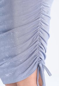 Světle modré šaty s řaseným designem po straně, vyrobené z jemné, elastické tkaniny, s detaily vázání na spodním lemu.