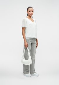 Λευκό τοπ με λαιμόκοψη V και διαφανείς μανίκες, γκρι παντελόνι με φαρδιά πόδια, λευκά αθλητικά παπούτσια και λευκή τσάντα με διακοσμητικές βίδες και καμπυλωτή λαβή.