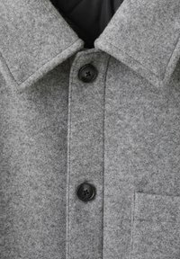 Giacca camicia in misto lana grigia con collo a punta, due bottoni neri e una tasca sul petto con una texture liscia.