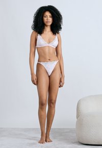 Set de lenjerie roz deschis cu accente de dantelă, compus dintr-un bralette triunghiular și un tanga asortat, ambele decorate cu modele florale mici.