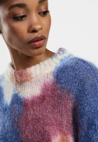Maglione lavorato a maglia multicolore con tonalità blu, rosa e bianco. Presenta una texture morbida e vellutata e un collo a coste.