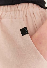 Svetlo ružové bavlnené šortky so zberovým pásom v páse, s bočnou vreckom a malou čiernou etikou s bielym grafickým detailom.