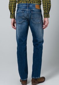 Jeans de mezclilla azul oscuro con corte recto, textura desvanecida, bolsillos traseros con detalle de costura y un parche de cuero con marca en la cintura.
