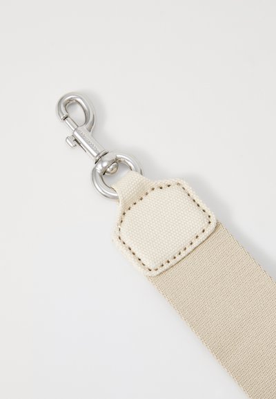 Beige tygrem med en silverfärgad metalclip, med en texturerad yta och en sydd lapp nära clipet.