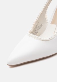 Λευκό παπούτσι μυτερό με διακοσμητικά μαργαριτάρια κατά μήκος του ανοίγματος και κείμενο τυπωμένο στο εσωτερικό της σόλας.