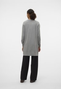 Gray long-sleeve top with a straight cut, featuring a round neckline and side slits, paired with black wide-leg trousers.