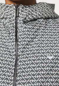 Svart och vit jacka med ett intrikat geometriskt mönster, dragkedjeslutning och hög krage med en slät yta.