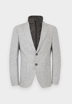 Grijze blazer met een gestructureerde afwerking, voorzien van een zwart gewatteerde ritsvoering, twee voorzakken en twee donkere knopen aan de voorkant.