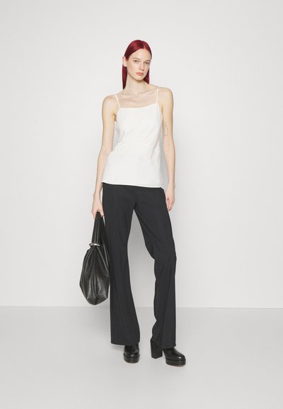 Top en camisole blanc avec des fines bretelles, associé à un pantalon large noir et des talons plateformes. Un sac noir à la main complète la tenue.