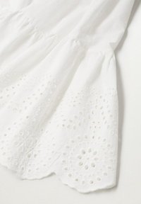 Weißes Baumwollkleid mit bestickten Lochmustern am Saum. Verfügt über Rüschendetails an der Naht, eine weiche Textur und einen gewellten Rand.