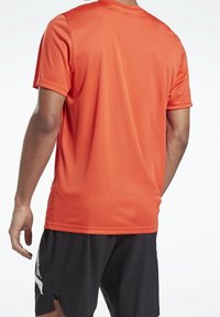 Camisa atlética de manga corta en naranja brillante, hecha de material suave y ligero. Presenta un cuello redondo clásico y un corte relajado.