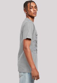 Camiseta de algodón gris con mangas cortas, que presenta un diseño gráfico en azul que representa montañas y vida salvaje en la parte delantera.