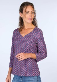 Lila Bluse mit V-Ausschnitt, die ein sich wiederholendes Blumenmuster in Pink und Blau aufweist. Dreiviertelärmel, aus leichtem Stoff gefertigt.