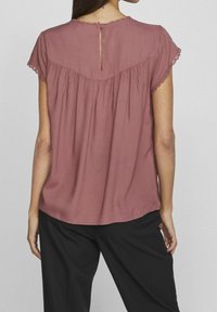 Blusa a maniche corte, dal fit morbido, in rosa polveroso con scollatura tonda, rifiniture all'uncinetto e dettaglio a chiave sul retro. Tessuto morbido.