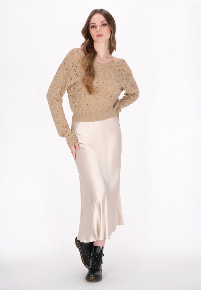 Suéter de punto beige con un corte holgado y detalles texturizados. Falda midi de seda crema con un ligero vuelo en el dobladillo. Botas negras con cordones.