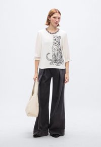 Λευκό πουκάμισο με μαύρο λεοπάρ μοτίβο, στρογγυλή λαιμόκοψη με λεπτομέρεια λεοπάρ, συνδυασμένο με άνετο σκούρο γκρι παντελόνι και μπεζ τσάντα.