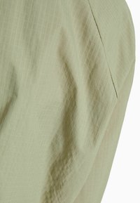 Light green textured fabric with a grid pattern, showing soft folds and seams, suggesting a lightweight and breathable design.