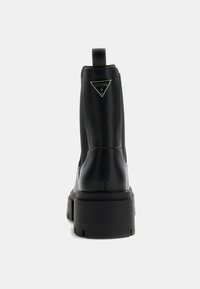 Botines negros con un diseño elegante, hechos de piel suave. Cuentan con una suela gruesa y un logo triangular en la parte trasera.