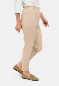 Pantalons beiges fuselés avec une taille élastique, une poche zippée sur le côté et un tissu texturé. Associés à des mocassins beiges détaillés avec des accents dorés.