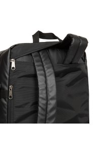 Mustakokoinen reppu, joka on valmistettu kestävästä nailonista, jossa on kaksi pehmustettua olkahihnaa ja useita vetoketjullisia taskuja turvallista säilytystä varten.