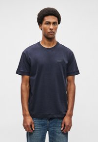 Μπλε ναυτικό βαμβακερό t-shirt με στρογγυλή λαιμόκοψη, κοντά μανίκια και ένα μικρό ορθογώνιο λογότυπο στο στήθος. Χαλαρή εφαρμογή και λεία υφή.