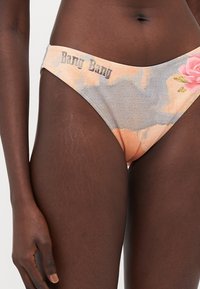 Bas de bikini en pêche et gris avec des motifs floraux, tissu texturé, et "Bang Bang" imprimé sur la taille. Présente des fines lanières sur les côtés.