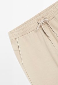 Beige joggings met een elastische tailleband, koordsluiting, zijzakken met witte bies, en een zachte, gestructureerde stof.