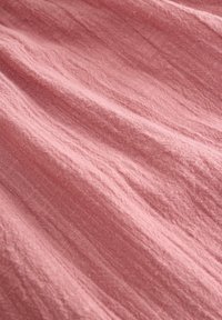 Hellrosa strukturiertes Gewebe mit leicht zerknitterter Oberfläche, das eine weiche, atmungsaktive Webart und ein natürliches, unregelmäßiges Finish zeigt.