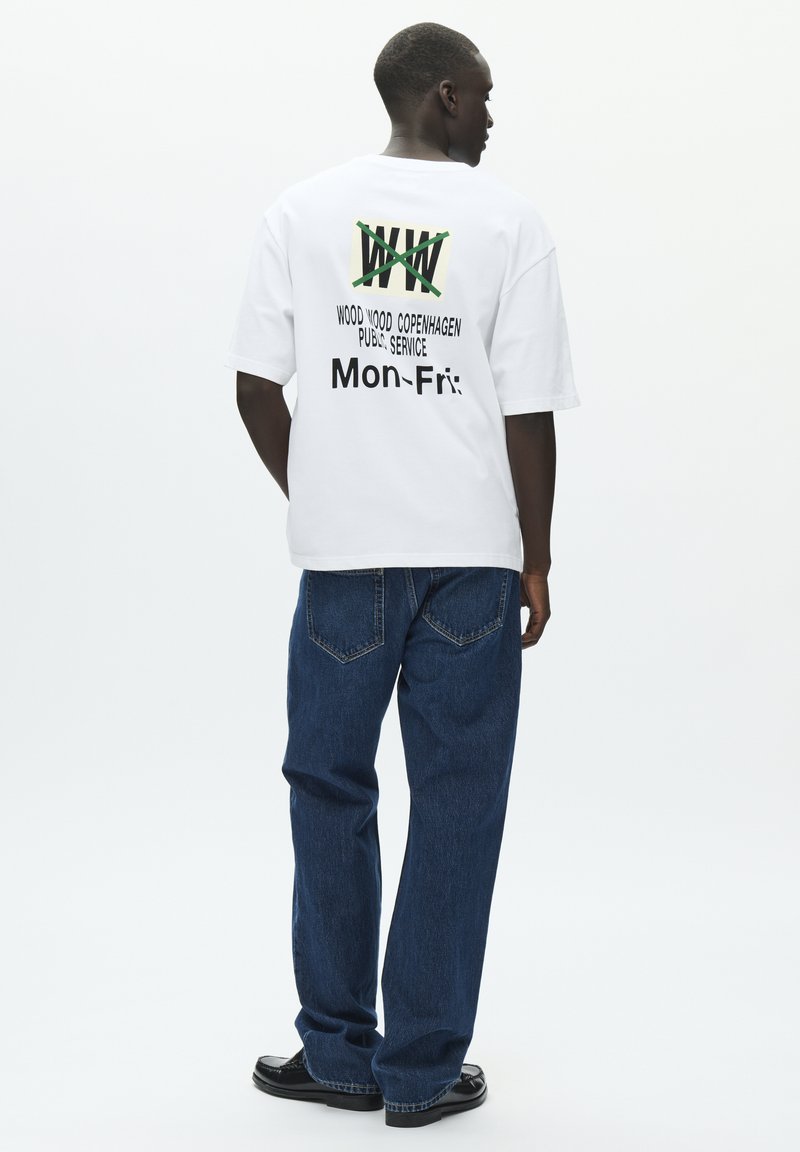 Hvit t-skjorte med grønn og svart tekst, med "Wood Wood Copenhagen" og "Man-Fre" trykt på baksiden. Kombinert med blå jeans.