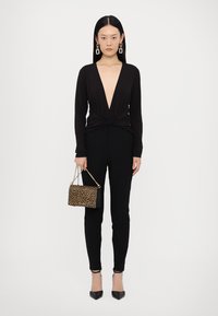 Černý dlouhý rukáv top s hlubokým V-výstřihem a twist detailem, spárovaný s černými skinny kalhotami. Celkový vzhled doplňuje leopardí kabelka.