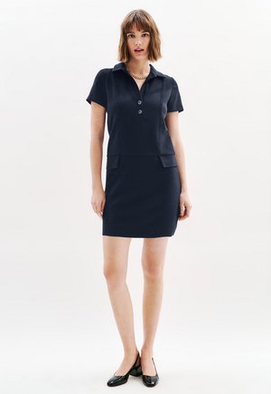 Abito polo in maglia di un blu scuro con maniche corte, patta con tre bottoni e una silhouette aderente, caratterizzato da una texture liscia e due tasche frontali.