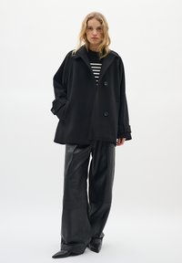 Black wool-blend coat with a notched collar and two buttons, paired with black leather wide-leg pants and a striped black-and-white top.