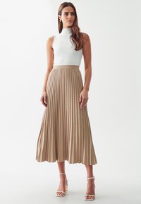 Gonna midi plissettata beige realizzata in tessuto leggero, abbinata a una maglietta bianca aderente senza maniche e tacchi bianchi con cinturino.