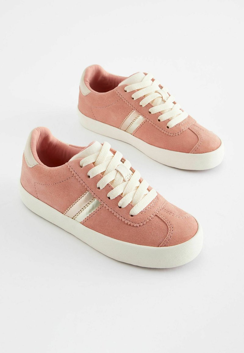 Zapatillas de ante rosa con cordones blancos, una superficie texturizada y franjas laterales blancas. Punta redondeada y suela plana de goma para uso casual.