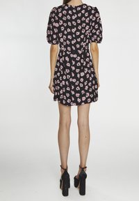 Vestido negro con un patrón floral en rosa, mangas cortas abullonadas, cintura ajustada y falda acampanada. Utilizado con tacones de plataforma negros.