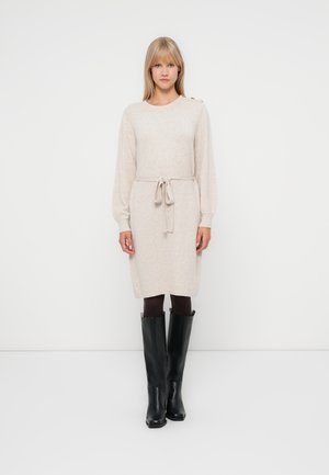 Lys beige strikket kjole med rund hals, lange ermer, belte i midjen og knapper på skulderen, kombinert med svarte støvler til kneet.