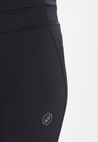 Czarne legginsy sportowe z wysokim stanem, gładką fakturą i kontrastowymi szwami. Logo jest widoczne na dolnej lewej nogawce.