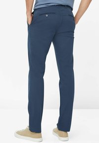 Granatowe bawełniane spodnie o prostym kroju, z dwoma tylnymi kieszeniami i zapięciem na guzik, w połączeniu z beżowymi trampkami.