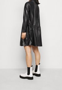 Svart konstläder klänning med långa ärmar och rynkad midja, kombinerad med vita ankellånga stövlar med svarta elastiska paneler och kraftiga sulor.