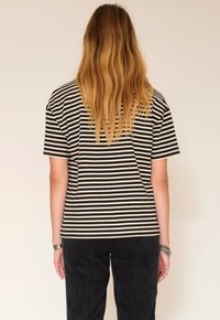 T-shirt à rayures noires et blanches avec manches courtes, coupe décontractée et col rond. Porté avec un pantalon en velours côtelé foncé.