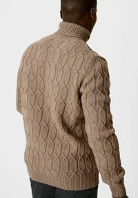 Beżowy sweter z dzianiny w splot warkoczowy z wysokim kołnierzem, ozdobiony teksturowanym wzorem w diamenciki. Materiał wydaje się miękki i gruby, idealny na chłodniejsze dni.