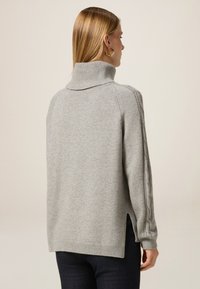 Jasnoszary sweter z dzianiny z wysokim kołnierzem, prążkowanymi detalami, bocznymi rozcięciami i akcentami w warkocze na rękawach. Miękka tekstura i luźny krój.