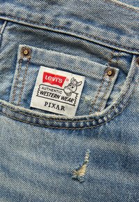 Jasnoniebieska tkanina dżinsowa z przetartym miejscem, z białą etykietą z czerwonym i czarnym tekstem "Levi's Authentic Western Wear" oraz rysunkowym logo.