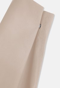 Tejido beige con una textura suave, que presenta dos paneles superpuestos y un acento metálico circular a lo largo del borde.