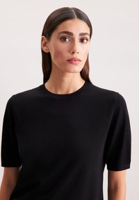 Czarny sweter z krótkim rękawem i okrągłym dekoltem, wykonany z miękkiego materiału, o gładkiej fakturze i bez widocznych wzorów czy akcentów.